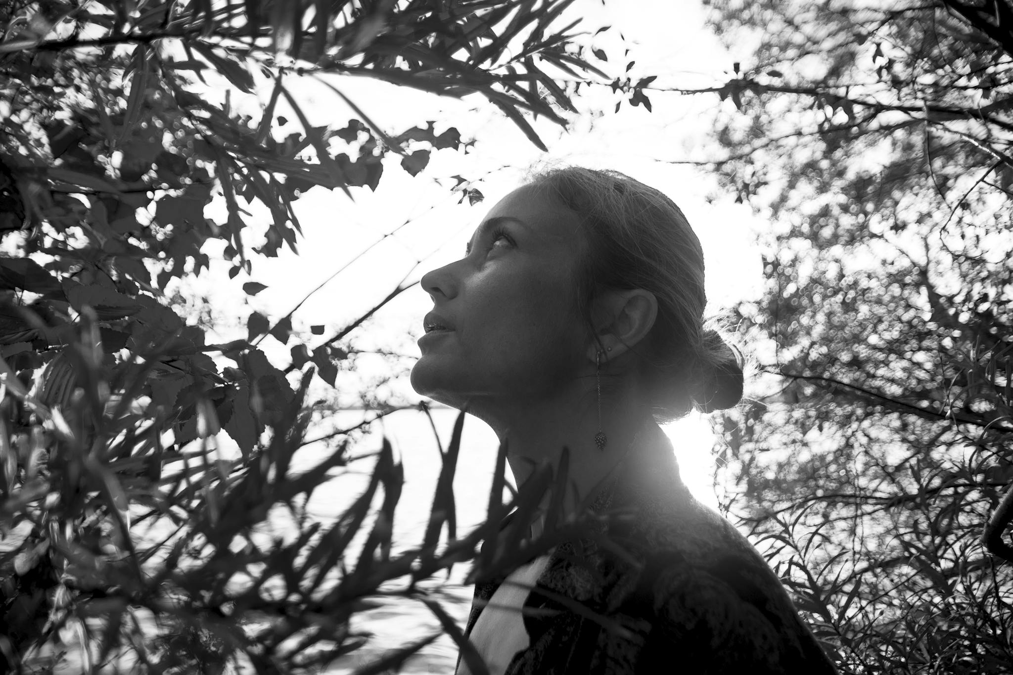Artistic black and white portrait of a woman admiring nature among trees with backlight.